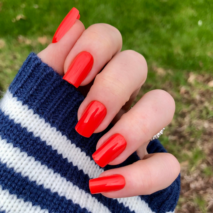 Lava - Press-On | Medium | Square showing hand outdoors with bright glossy spicy orange-red medium square false nails