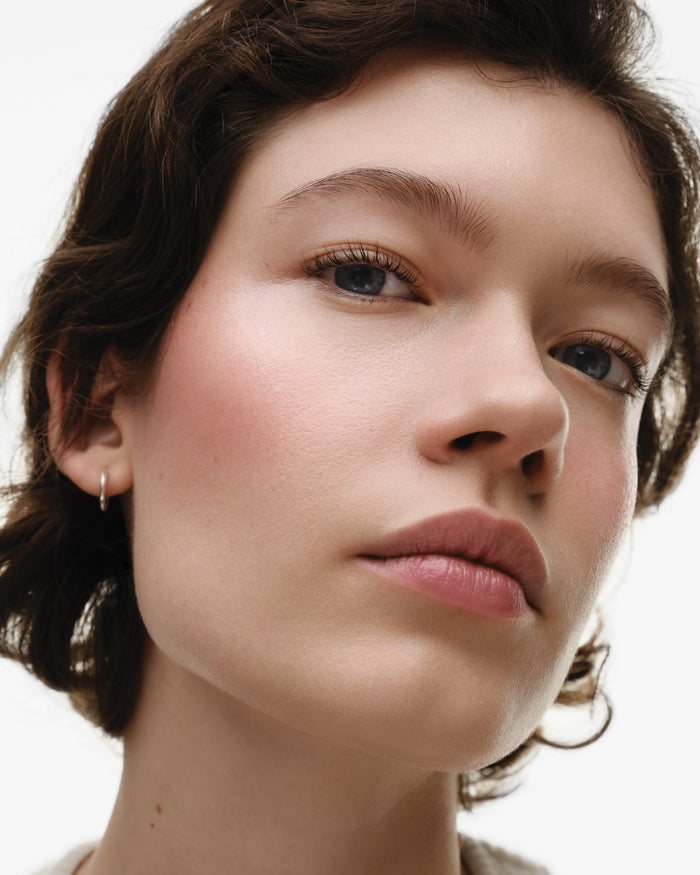 Close-up of a woman with a neutral expression, rosy cheeks and a plain background