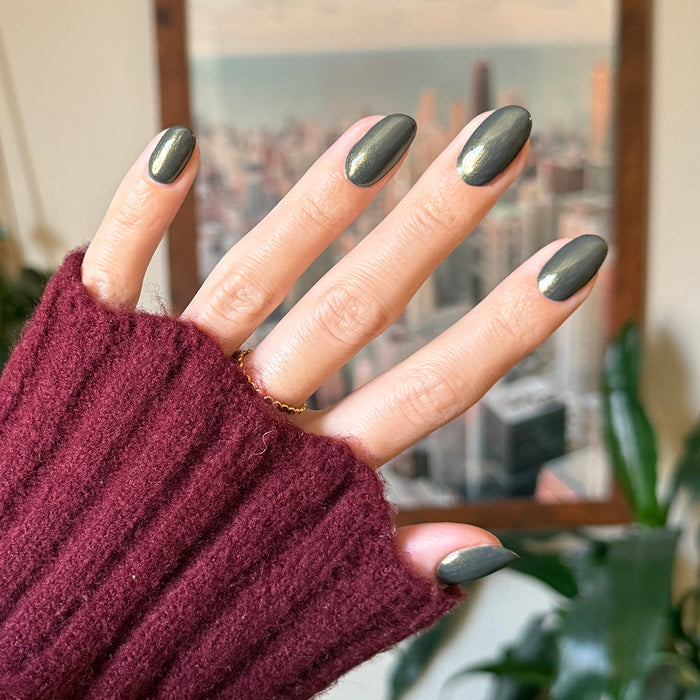 Hand with medium-length nails painted in Martini Chrome gel polish showing deep olive green with golden chrome shimmer manicure