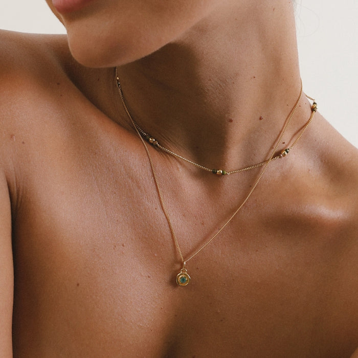 Close-up of a person wearing a gold necklace with a green gemstone pendant on a neutral background