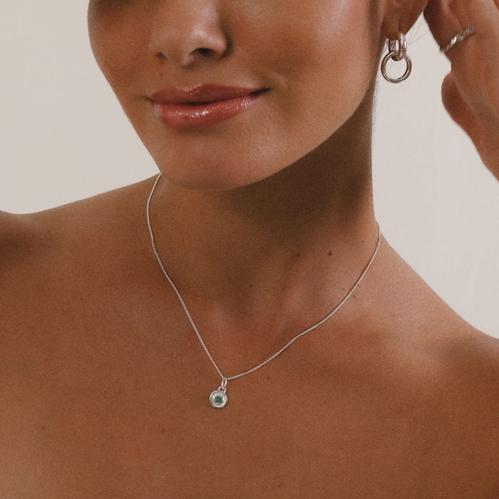 Close-up of a woman wearing a silver necklace and earrings on a neutral background