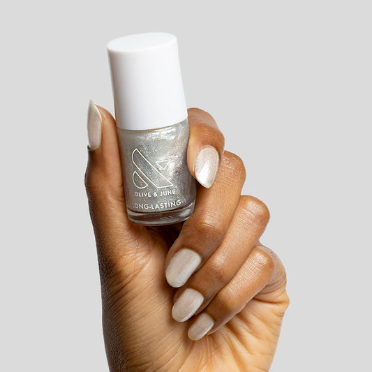 Hand holding Olive and June Midnight Disco quick dry polish bottle with shimmering silver glitter manicure on nails