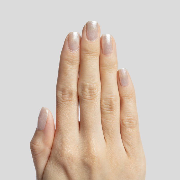Hand with short natural nails wearing subtle shimmer polish in Midnight Disco by Olive and June against light gray background