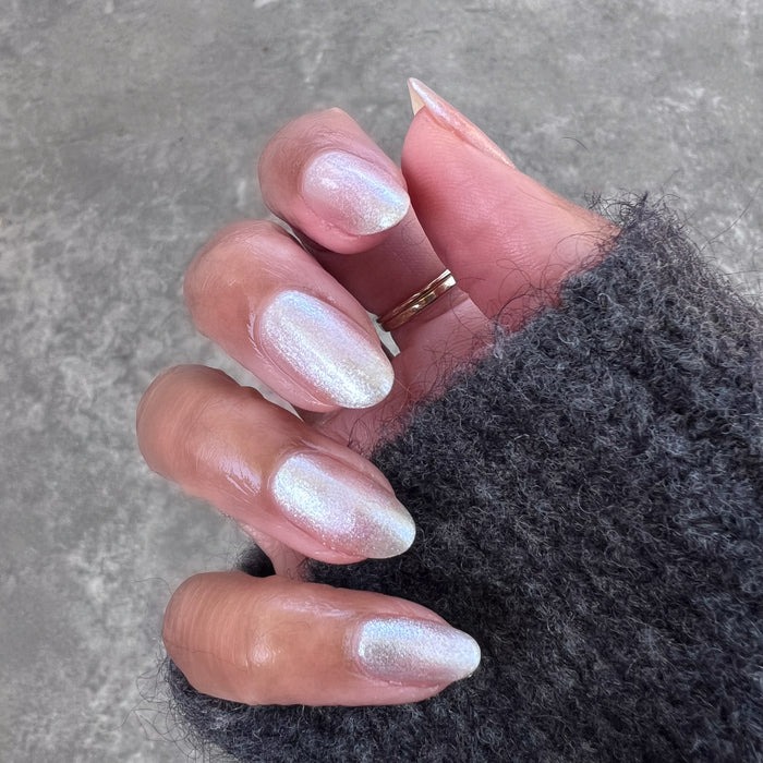 Hand with medium-length natural nails painted in shimmering Midnight Disco polish against gray background