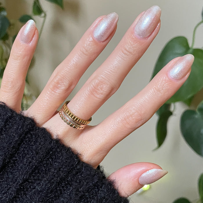 Hand with almond-shaped nails featuring subtle shimmer manicure in Midnight Disco polish against plant background