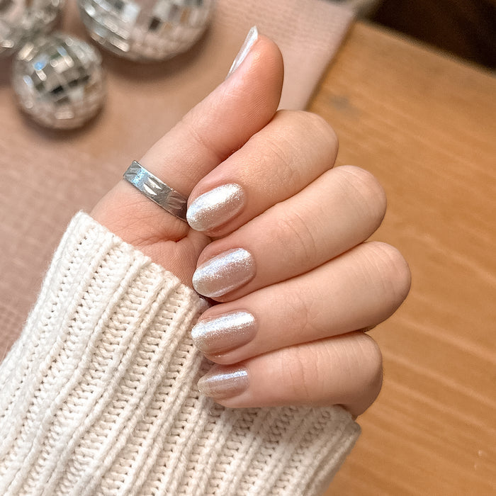 Hand with short oval nails in a shimmering mani featuring Midnight Disco polish by Olive and June against neutral background