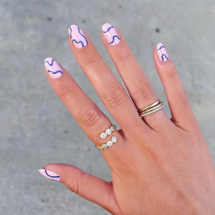 Hand with nails featuring abstract blue lines on pale pink, showcasing manicures done with Nail Art Brush Set