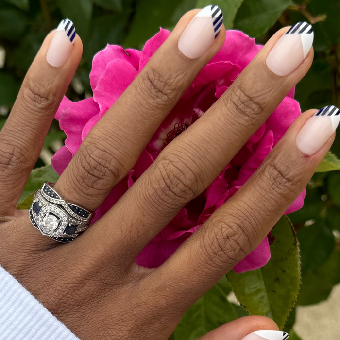 Nautical Split French - Press-On | Medium | Oval press-on nails with navy striped french tips on hand over pink flower background
