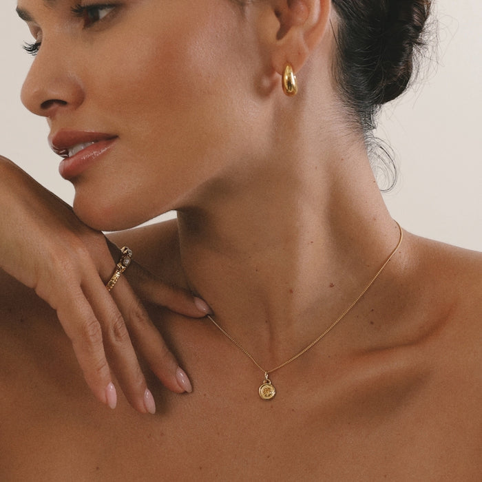 Close-up of a woman wearing gold jewelry including earrings, necklace, and ring.