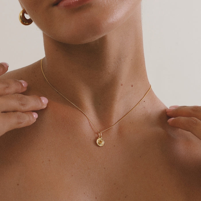 Close-up of a person wearing a gold necklace with a small pendant on a neutral background