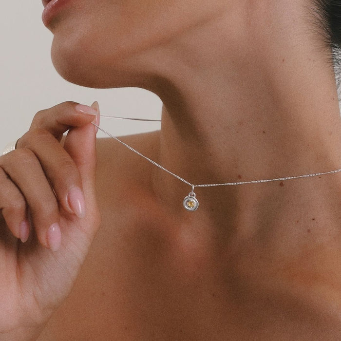 Person adjusting a delicate necklace with a small pendant.