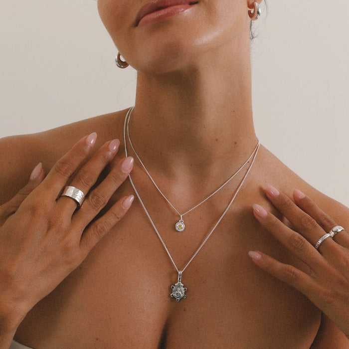 Woman wearing two silver necklaces with pendants, one of which has a small round gemstone.
