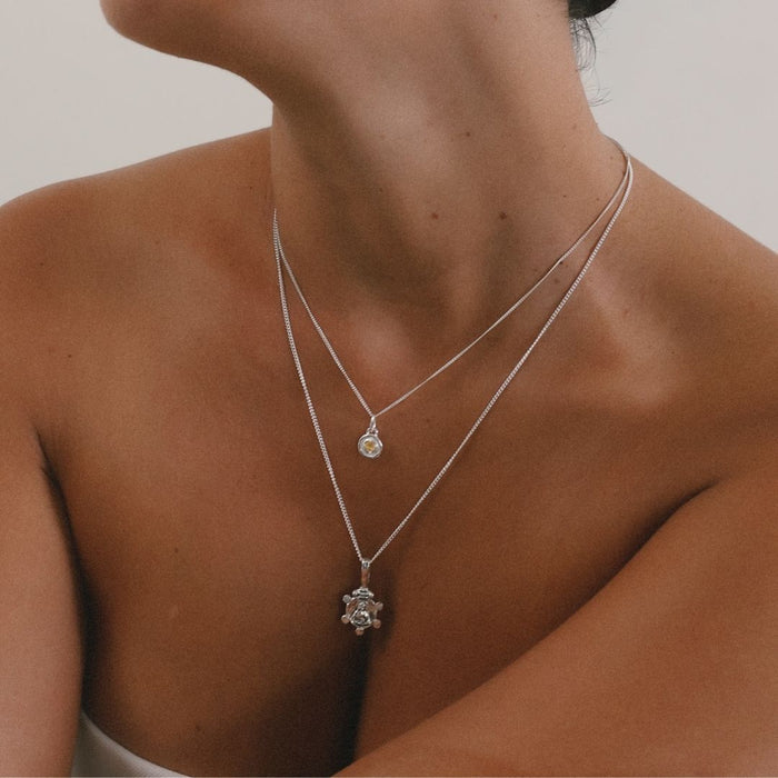 Close-up of a person wearing two silver necklaces with pendants on a neutral background