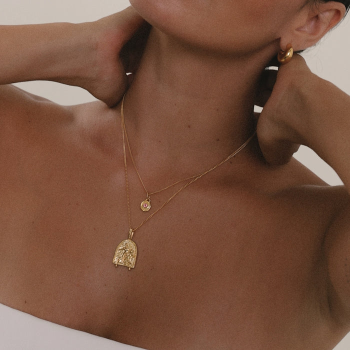 Close-up of a person wearing gold necklaces and earrings on a neutral background
