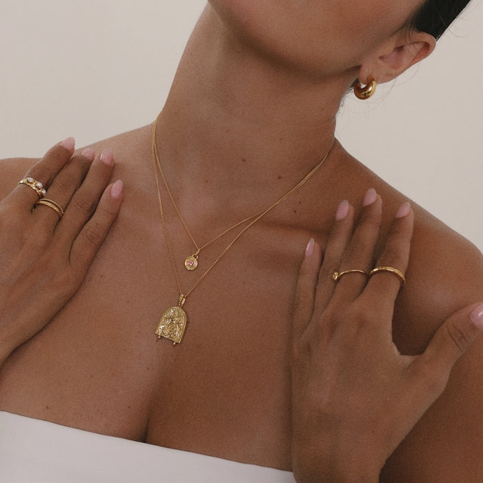 Close-up of a person wearing gold jewelry including a necklace, earrings, and rings.