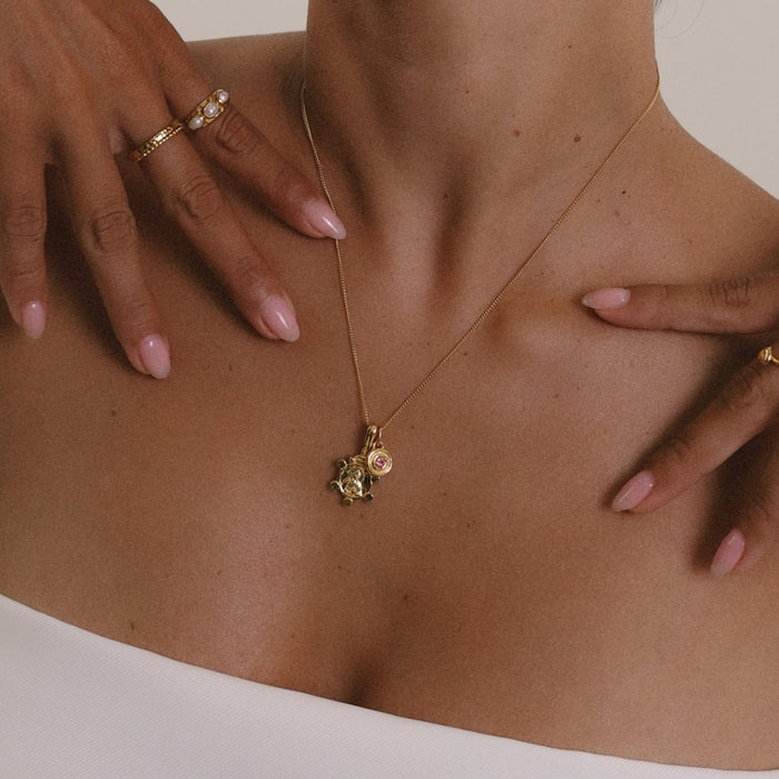 Gold necklace with a pendant on a person's neck, with hands gently touching the skin.