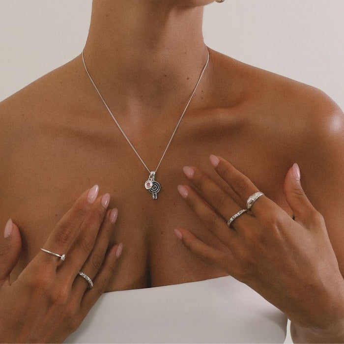 Person wearing a silver necklace with a pendant, surrounded by hands wearing rings.