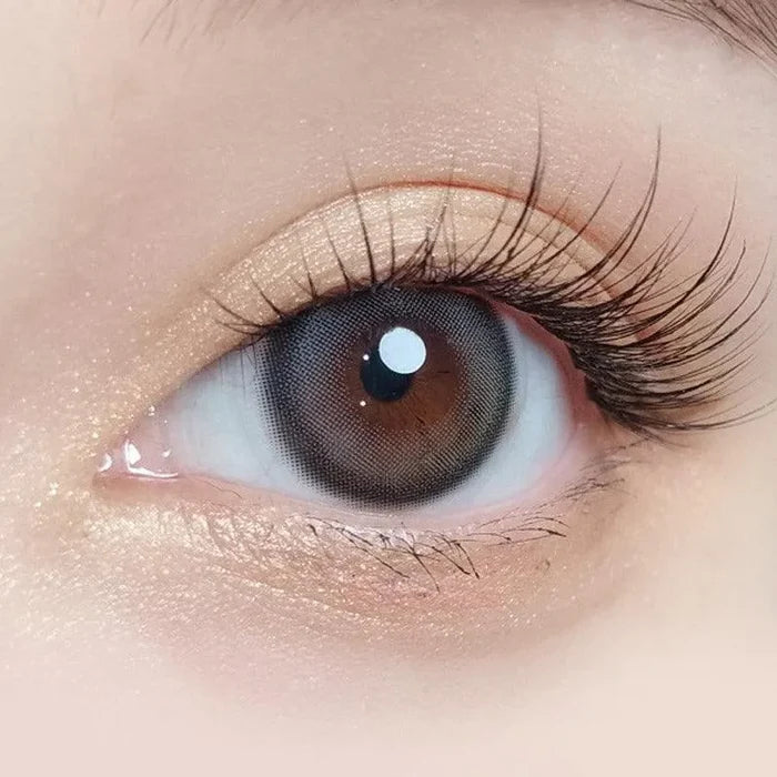 Macro shot of an eye wearing the Olola Blurring Grey prescription colour contact lens, showing the multi-colored detail and natural effect on dark brown eyes.
