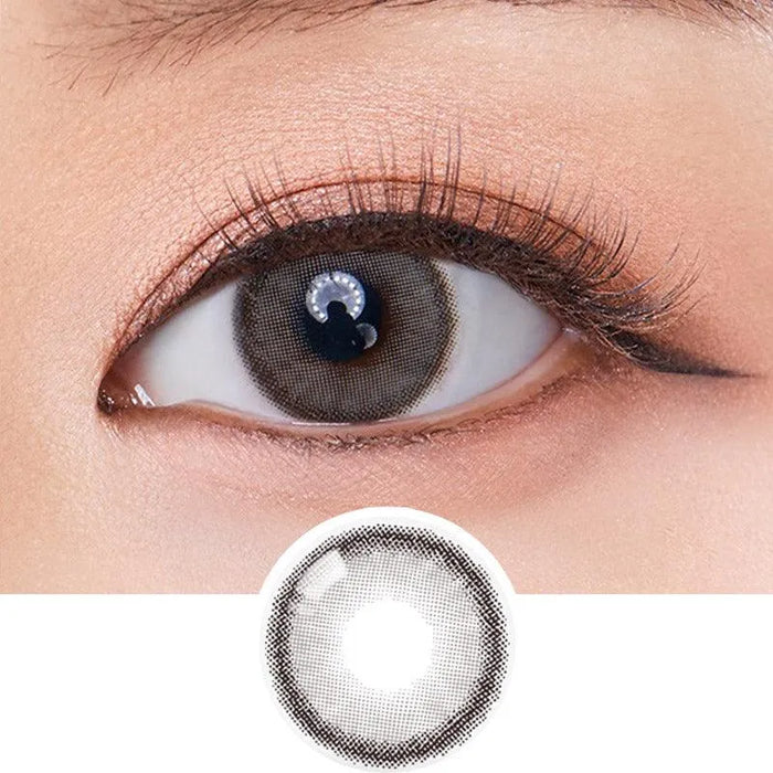 A close-up of an eye wearing Olola Dearsome Ash Grey contact lenses by Olola, ideal for dark eyes with long lashes and subtle makeup. Below the eye is an enlarged view of the same grey lens.