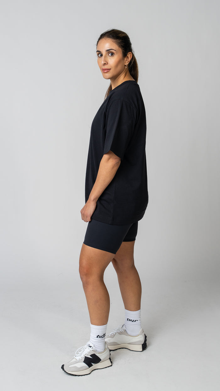 Woman wearing a plain white t-shirt and dark tights on a light gray background. Side View.