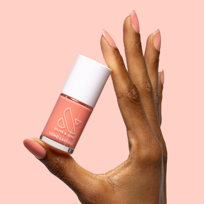 Hand holding Papaya Gloss nail polish bottle with sheer coral pink manicure on medium almond-shaped nails