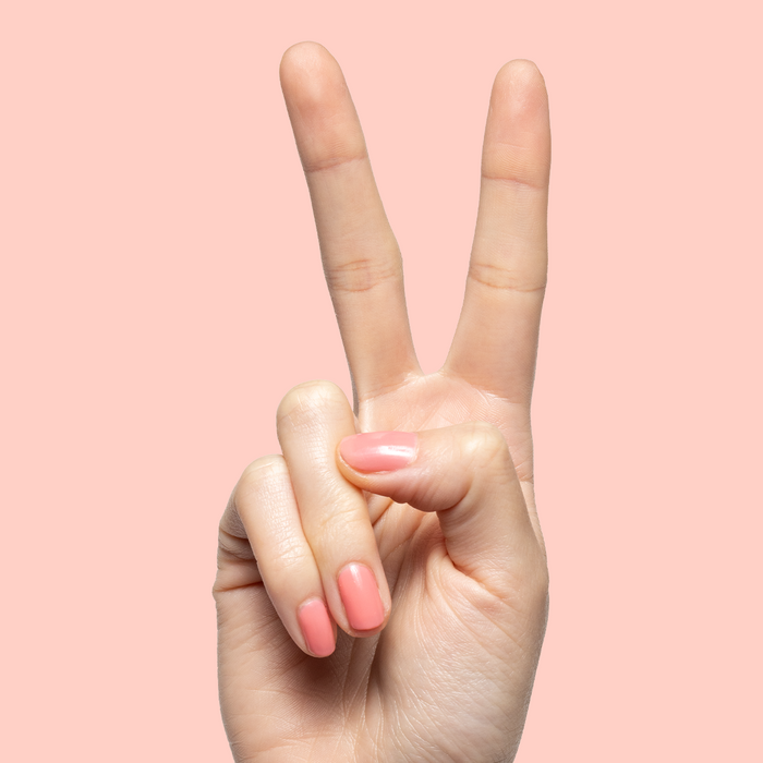 Hand showing peace sign with short nails painted in sheer coral pink using Papaya Gloss polish on peach background