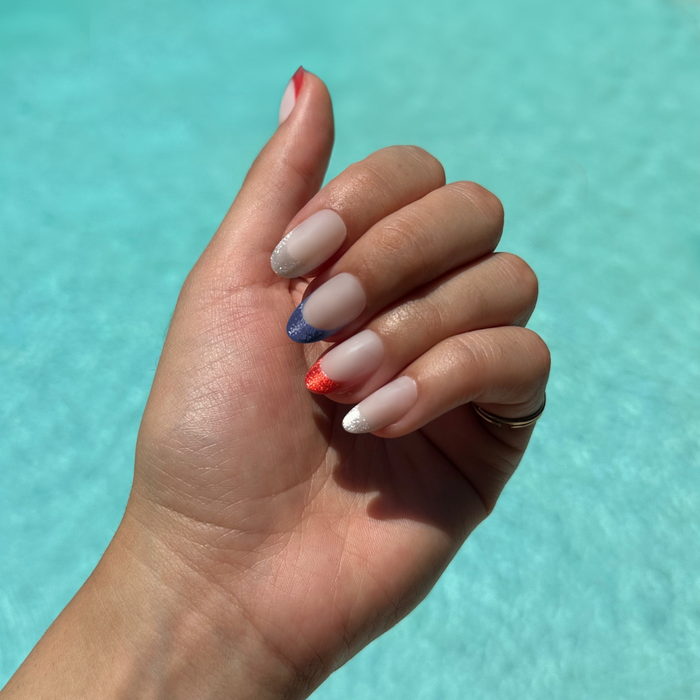 Parade Velvet French - Press-On | Medium | Oval showing milky base with red, blue, and white velvet tips manicure on hand outdoors