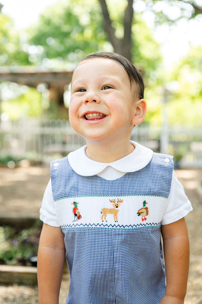 Baby boy smiling in Smocked Hunting Jon Jon by Ruth and Ralph, blue gingham with smocked deer and duck embroidery