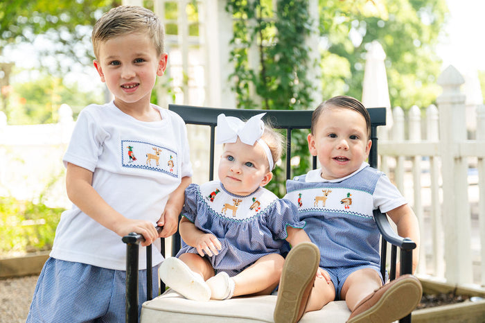 Three children outdoors, boy wearing Smocked Hunting Jon Jon by Ruth and Ralph with two siblings in matching smocked outfits"