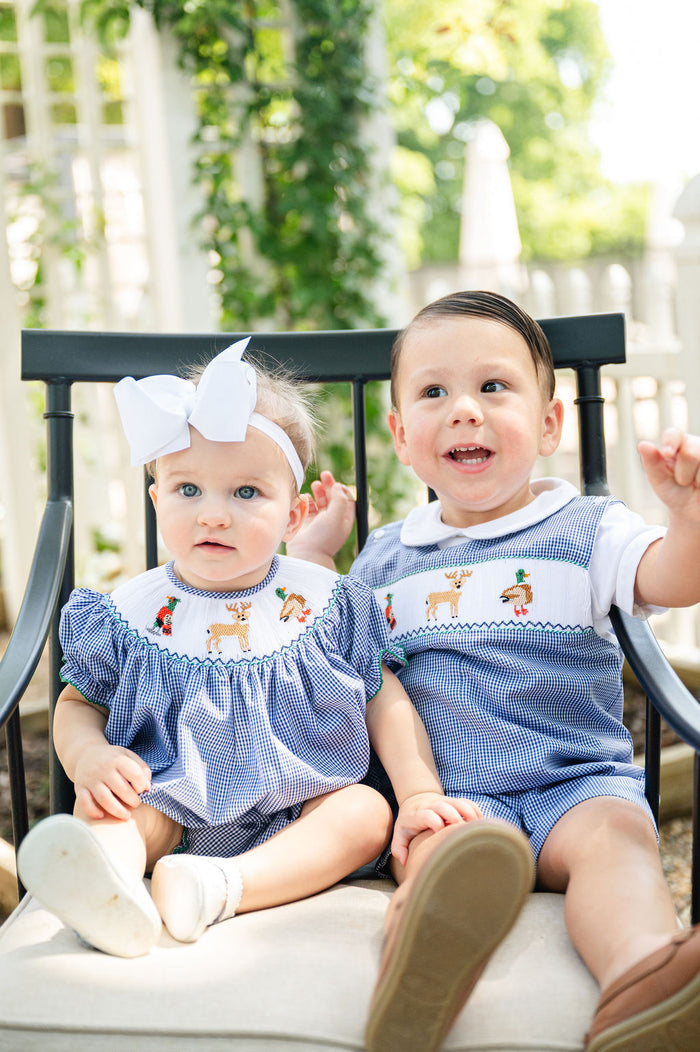 Baby girl and boy sitting together outdoors, boy wearing Ruth and Ralph Smocked Hunting Jon Jon with bow-topped sibling