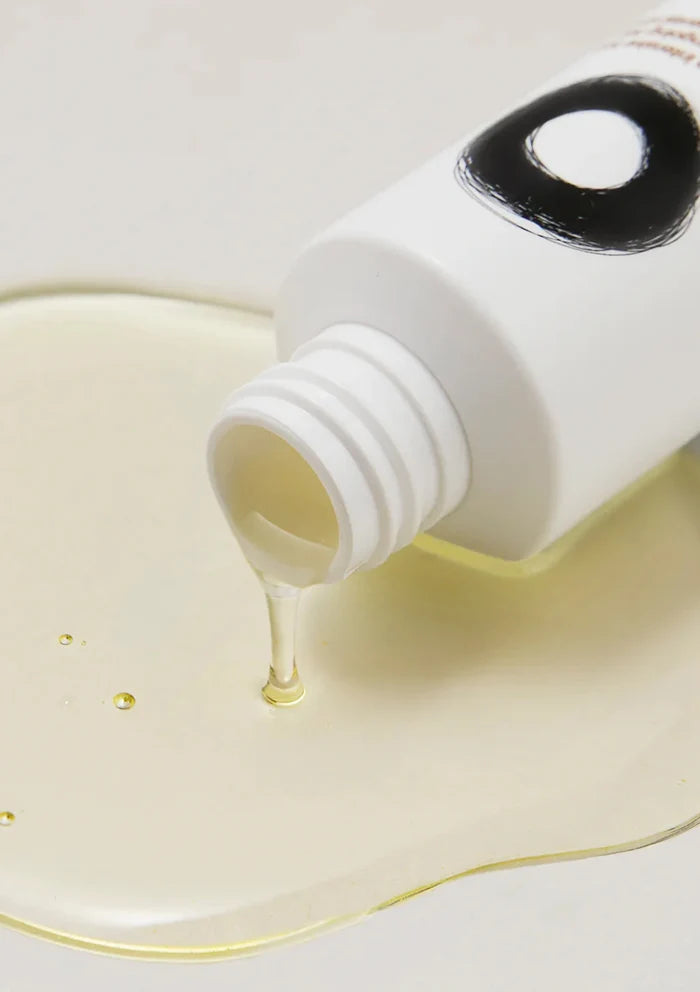 White bottle with a black cap pouring a yellow liquid onto a white surface.