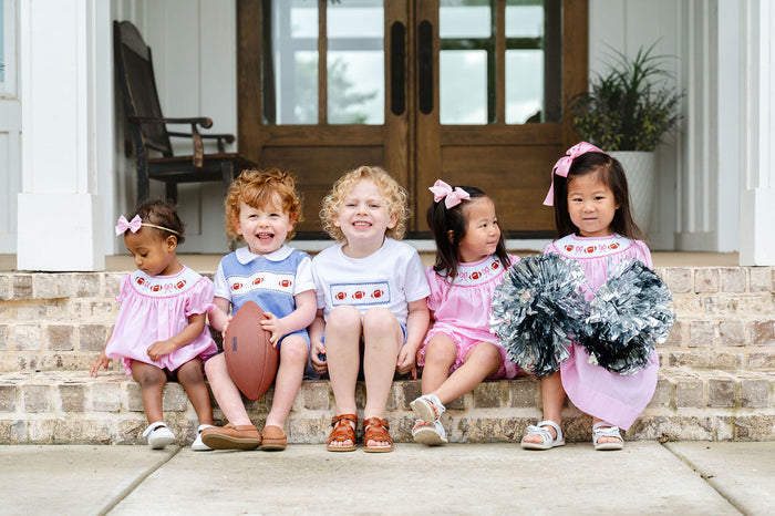 Group of children in coordinating game day smocked styles featuring hand-smocked footballs and bows