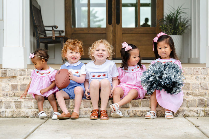 Group of children in coordinating game day smocked styles featuring hand-smocked footballs and bows