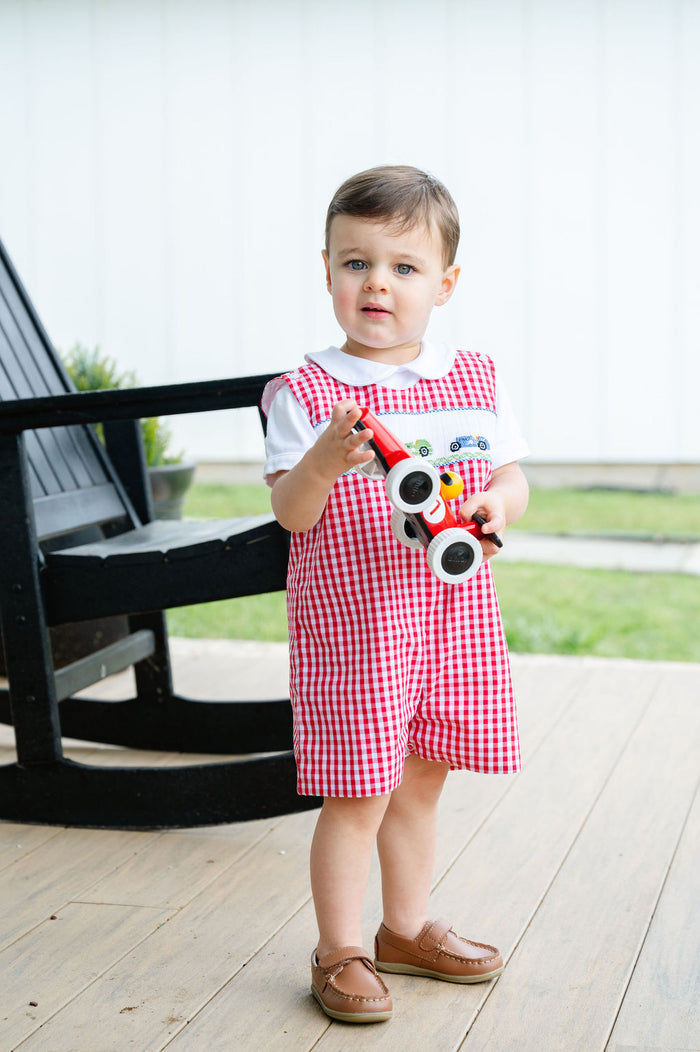 Baby boy standing on porch wearing Smocked Race Car Jon Jon by Ruth and Ralph, red gingham, holding toy