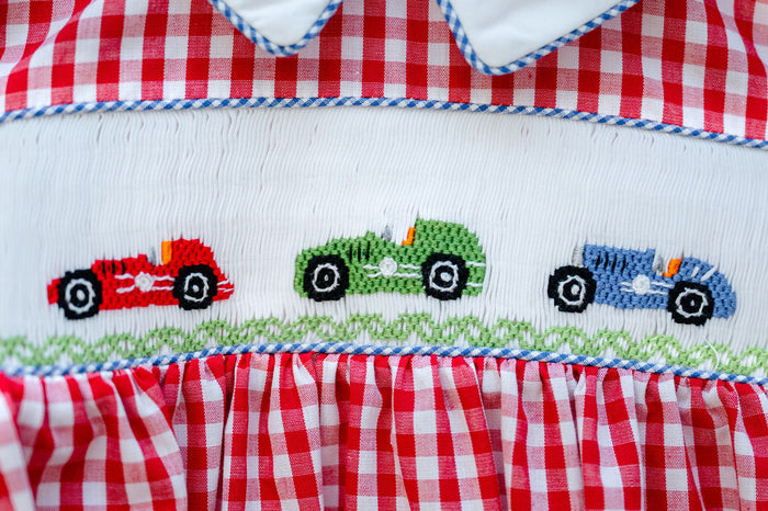 Close-up of smocked race car embroidery detail on Ruth and Ralph red gingham Bubble