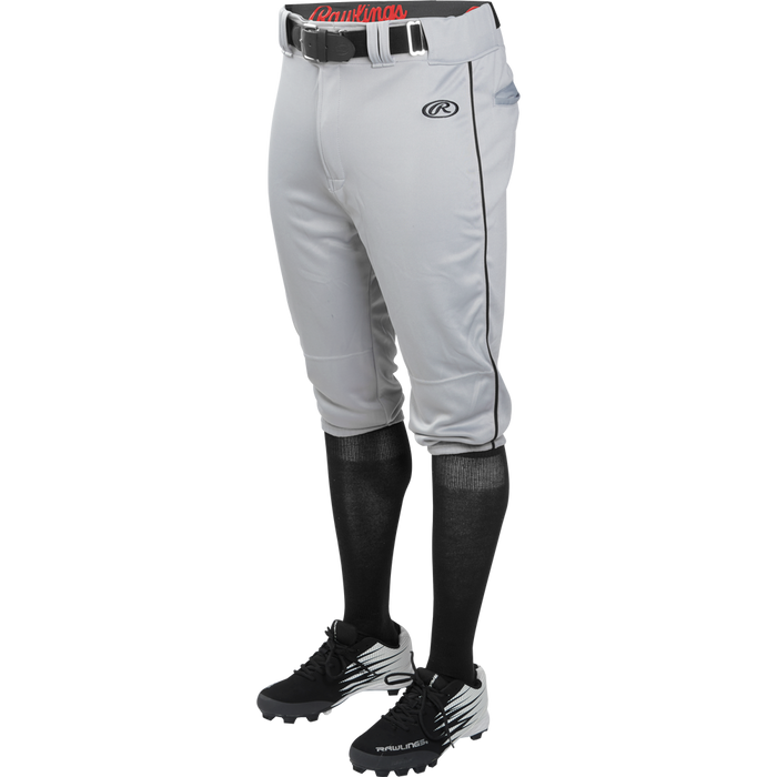 A person wears Rawlings Youth Launch Knicker Baseball Pants with Piping (gray with black piping), plus a black belt, black knee-high socks, and black cleats, shown waist down against a plain background.