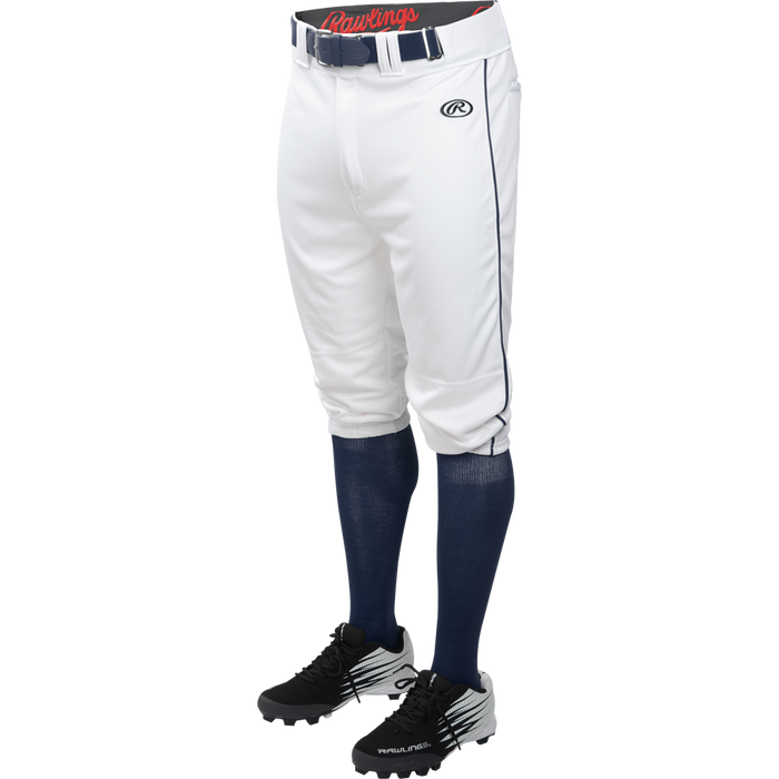 A person shown from the waist down wears Rawlings Youth Launch Knicker Baseball Pants with blue piping, a belt, navy socks, and black Rawlings cleats, all against a plain white background.