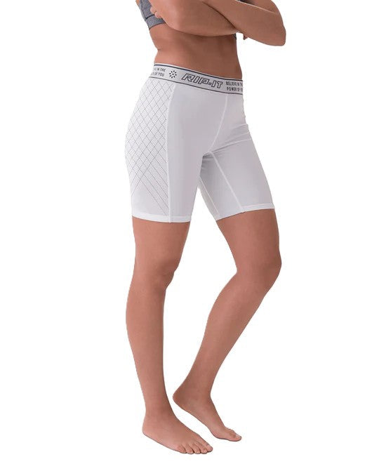 A person stands barefoot wearing Rip It Women's Period-Protection Pro Softball Sliding Shorts: 333000, featuring a diamond pattern on the side, branded elastic waistband, mid-thigh length, and built-in period protection. The upper torso and head are not visible.