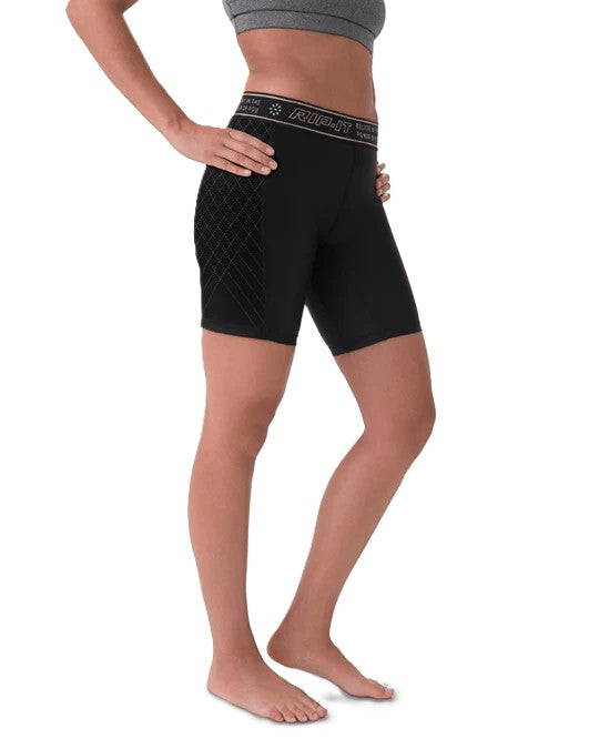 A person stands barefoot with hands on hips against a white background, wearing a gray sports bra and Rip It Women's Period-Protection Pro Softball Sliding Shorts: 333000, featuring quilted side panels.