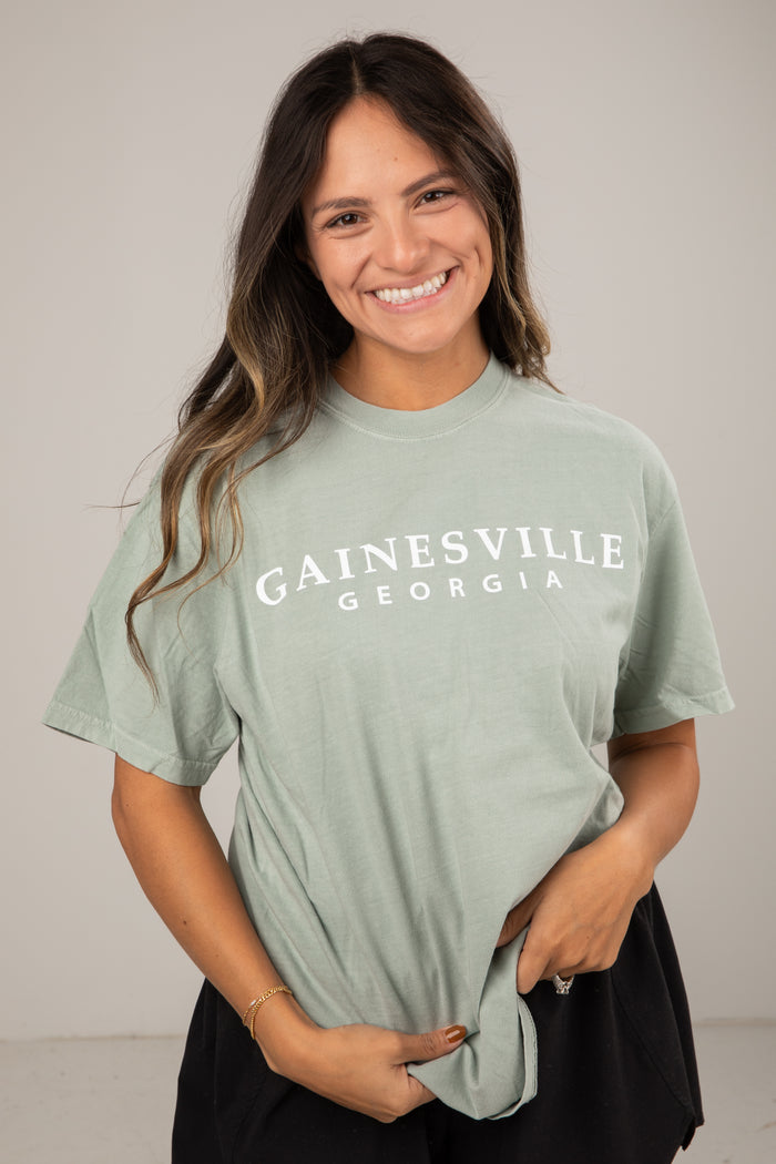 Woman wearing a light green t-shirt with 'Gainesville Georgia' text on a plain background