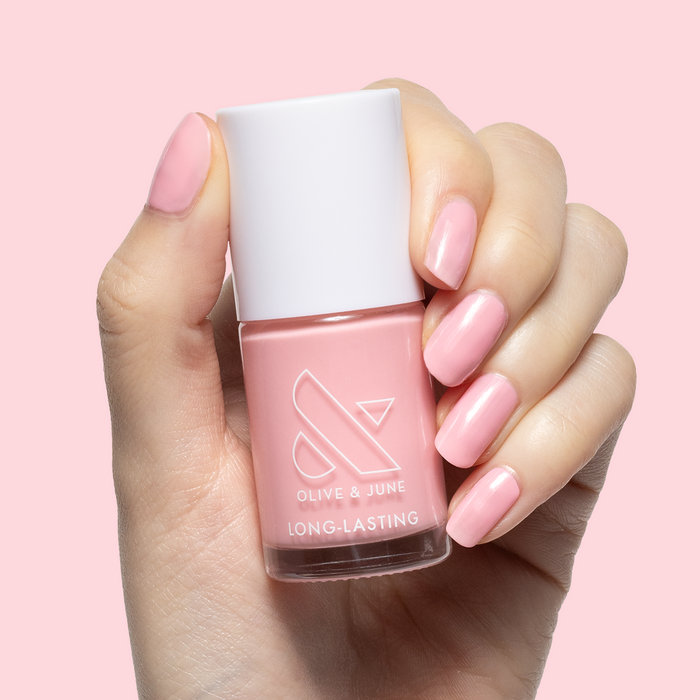 Hand with nails painted in soft pink Saltwater Taffy gel polish holding matching Olive & June polish bottle