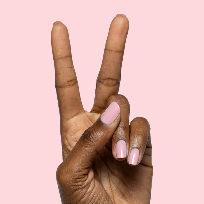 Hand with nails painted in sheer pink Saltwater Taffy gel polish showing polished manicure against pink background