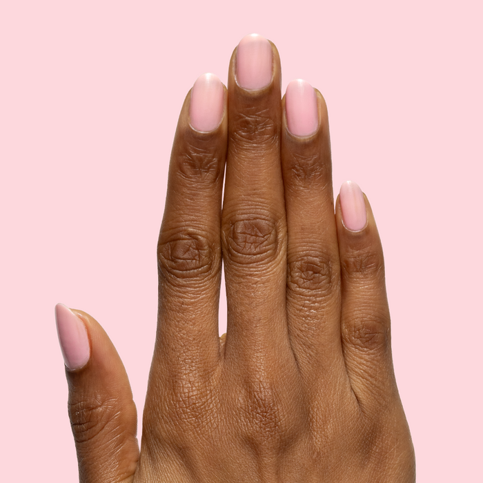 Hand with nails polished in sheer pink Saltwater Taffy gel polish showing smooth, natural manicure against light pink background