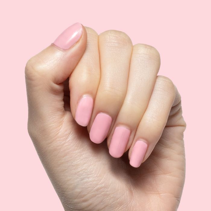 Hand with nails painted in sheer pink Saltwater Taffy gel polish showing smooth mani against pale pink background