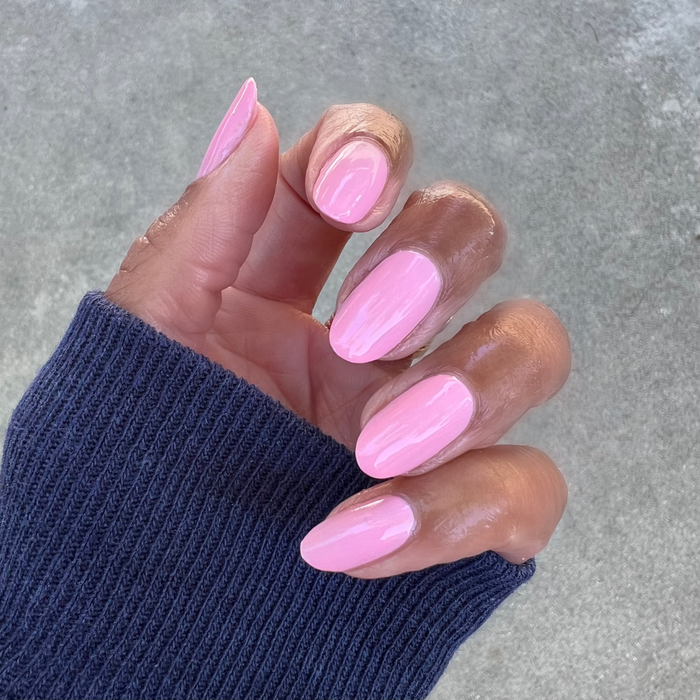 Hand with nails painted in sheer pink Saltwater Taffy gel polish showing glossy manicure against neutral background