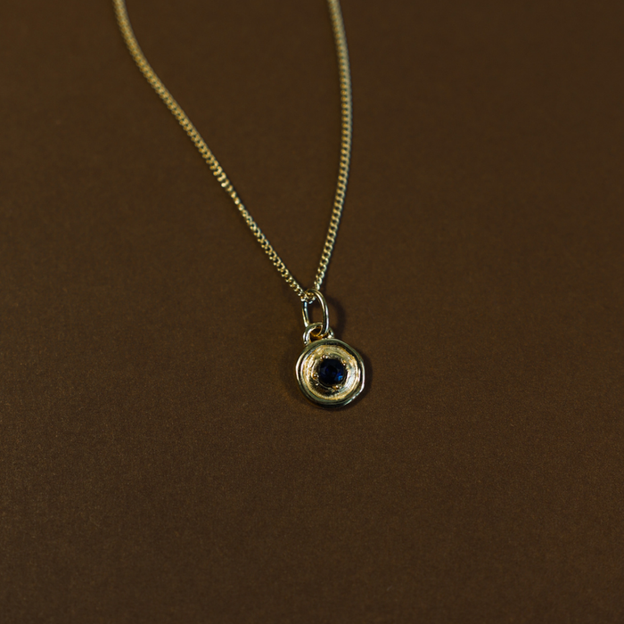 Gold necklace with a pendant featuring a blue gemstone on a brown background