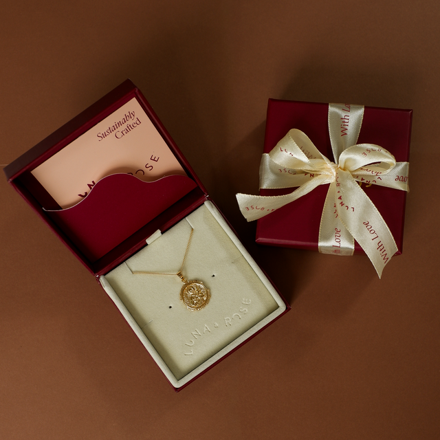 Gold necklace in an open jewelry box with a closed gift box featuring a ribbon on a brown background.