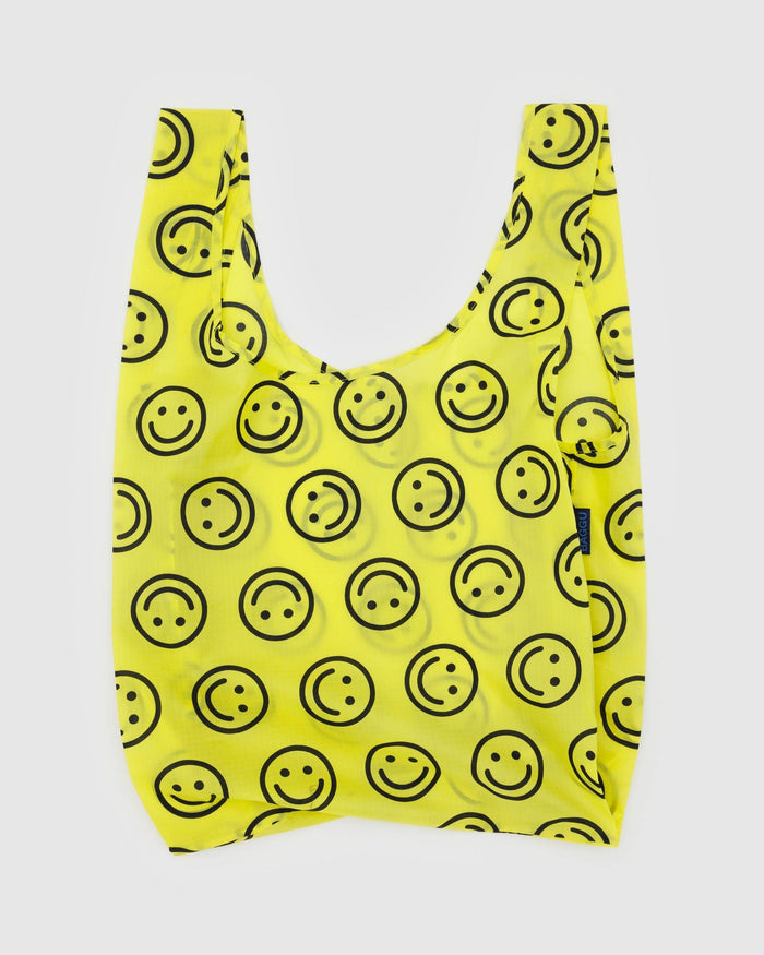 Reusable tote bag in bright yellow with smiley-face print and short U-shaped handles.