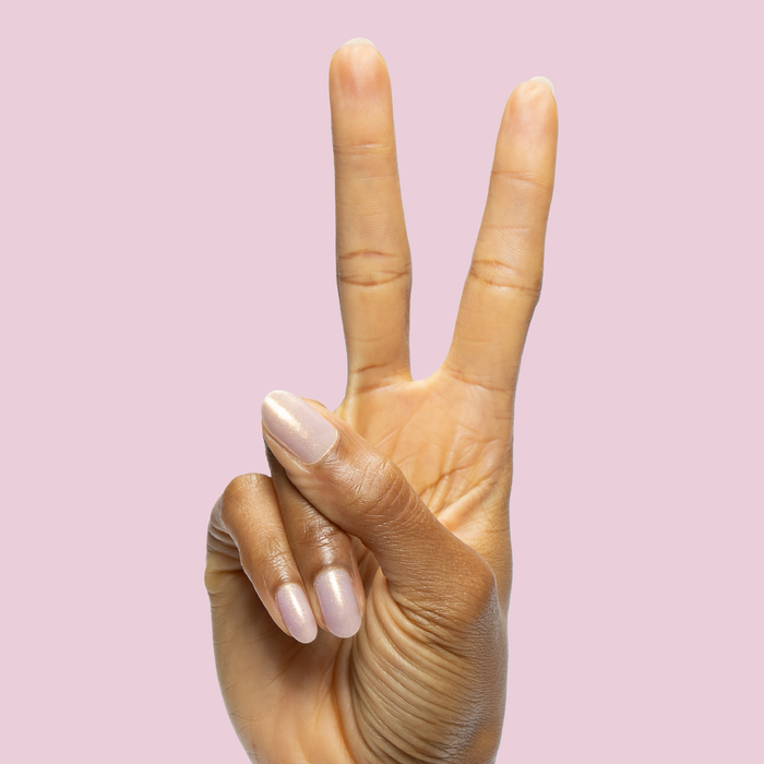 Hand with medium-length nails in Star Baker sheer iridescent lavender gel polish making a peace sign on light pink background