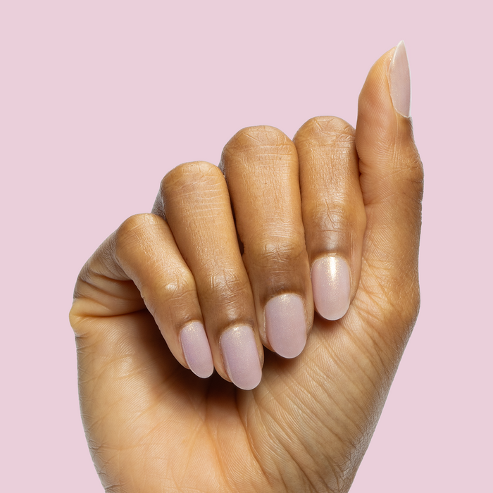 Hand with short oval nails polished in Star Baker sheer iridescent lavender gel polish on a pale pink background
